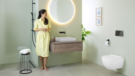 Woman in yellow dress standing in front of mint green bathroom with furniture and bathroom ceramics from Geberit and black taps